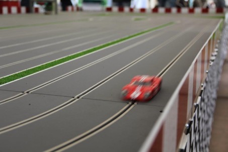 Ein rotes Miniaturauto f&auml;hrt auf einer Slotcarbahn.