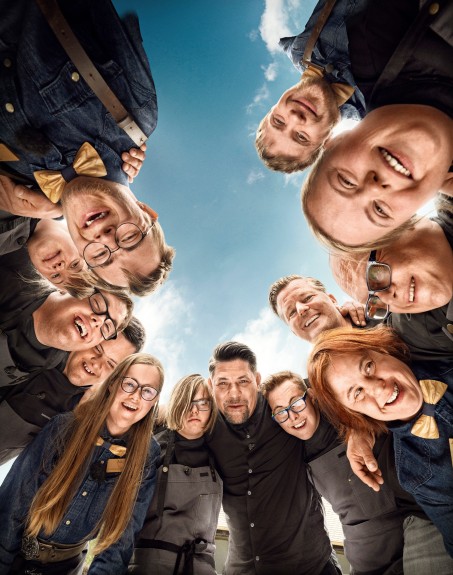 Man sieht Tim M&auml;lzer und das Team des Restaurants &quot;Zum Schwarzw&auml;lder Hirsch&quot;. Die Mitglieder des Teams leben mit Down-Syndrom. Alle Menschen auf dem Bild tragen schwarze Kleidung.