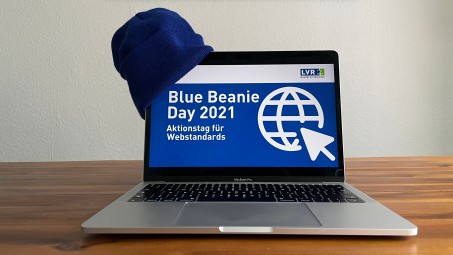 Ein aufgeklappter Laptop mit einer blauen M&uuml;tze seitlich auf dem Bildschirm