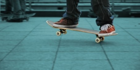 Man sieht zwei F&uuml;&szlig;e, die auf einem Skateboard stehen.