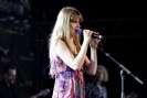 Eine Frau mit langen blonden Haaren steht auf einer B&uuml;hne und singt in ein Mikrofon. Sie tr&auml;gt ein buntes Sommerkleid.